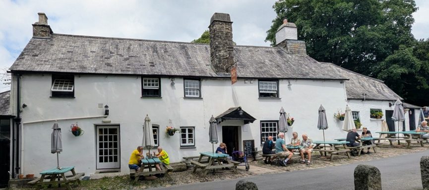 Traditional white cottage with a slate roof, featuring outdoor seating and seasonal decorations.