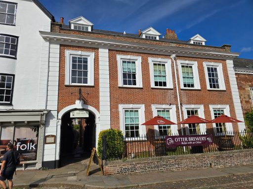 Historic brick building with white accents, outdoor seating, and shopfront nearby.