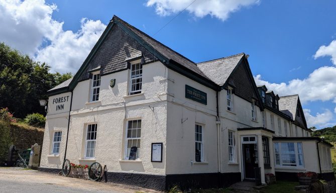 Historic three-storey building with a gabled roof and white exterior, surrounded by greenery.