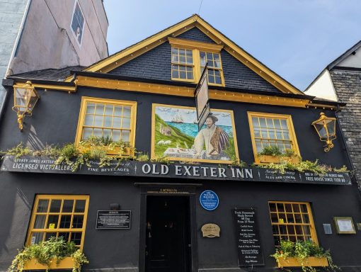 Black and yellow building featuring a mural and floral decoration, labelled "Old Exeter Inn."