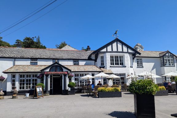 White pub building with a thatched roof and outdoor seating in a sunny, clear setting.