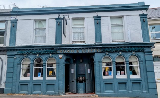 A traditional pub with a blue exterior and arched windows, located on a street.