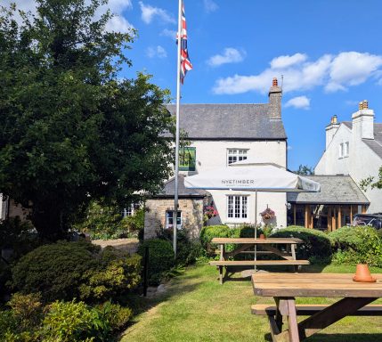 A garden with picnic tables, a flagpole, and a quaint building under a clear blue sky.
