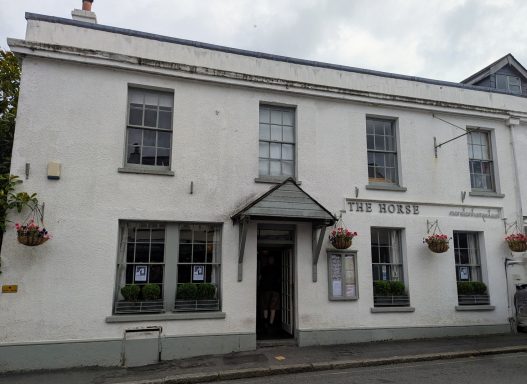 White building with large windows and a central entrance, featuring hanging flower baskets.