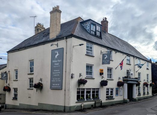 A traditional pub with a white exterior and flags, featuring hanging flower baskets.