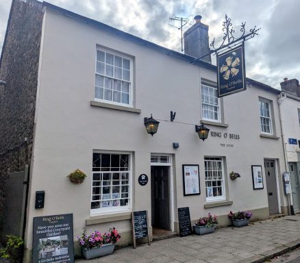 White-walled pub with a sign, flowers, and a menu board outside.