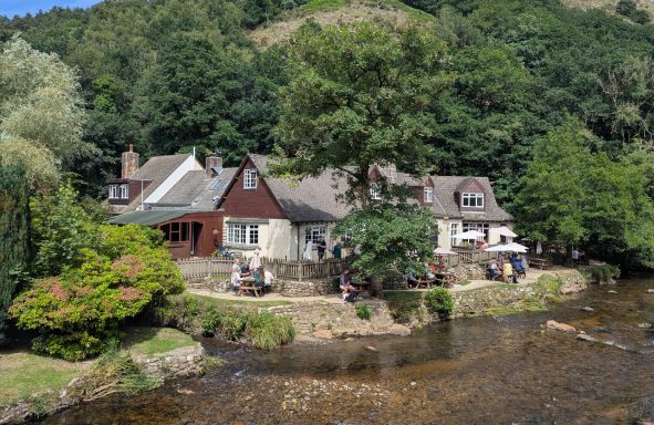 Cottages by a river, surrounded by lush greenery and people enjoying the outdoors.