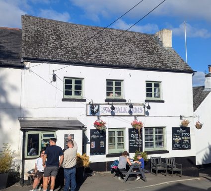 A quaint white pub with hanging flower baskets and outdoor seating, on a sunny day.