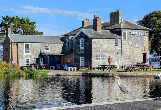 A historic building by the water with outdoor seating and a clear blue sky.