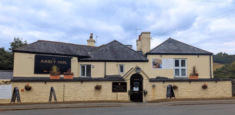 A traditional building with a light exterior, featuring signs and potted plants.