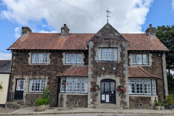 Historic stone building with large windows, traditional roof, and decorative wall plants.