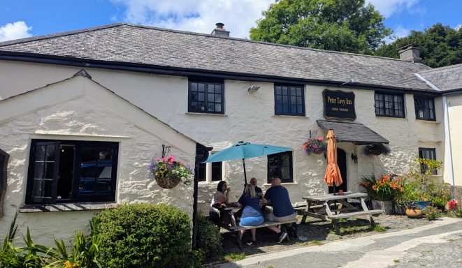 A quaint pub with outdoor seating and patrons socialising under an umbrella.