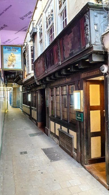 Narrow corridor with a wooden pub exterior and a bright poster overhead.