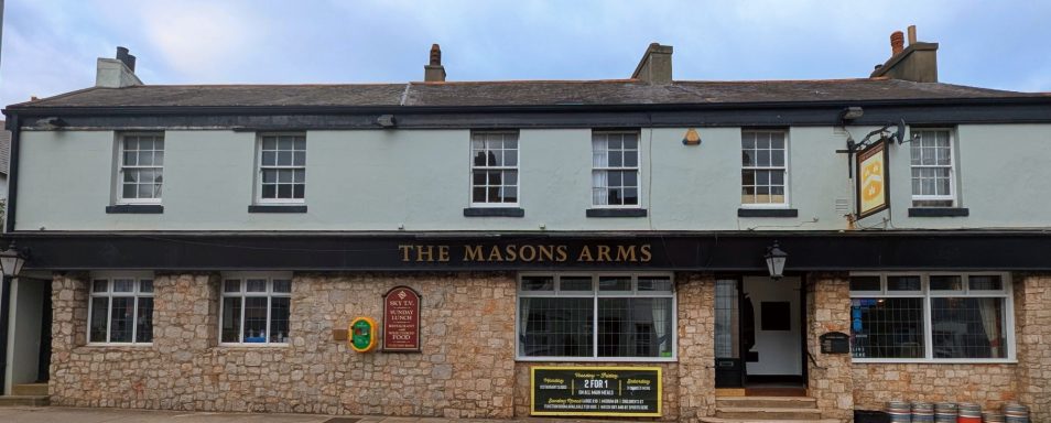 A traditional pub with light green and brick exterior, featuring large windows.