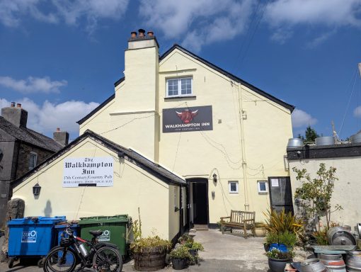 Yellow building with a sign for a bar, surrounded by bins and plants.
