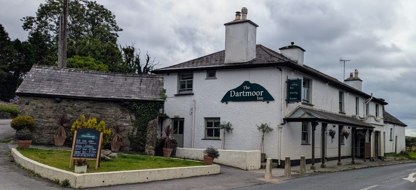 A traditional white building with a dark roof, featuring a pub sign and surrounding greenery.