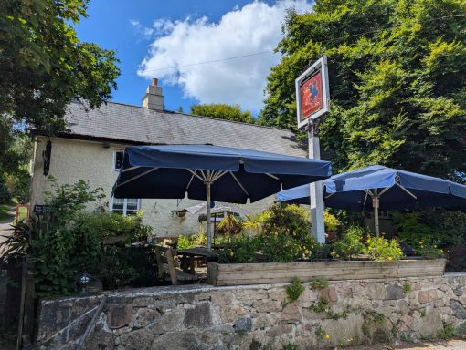 A quaint pub with blue awnings and lush greenery, under a partly cloudy sky.