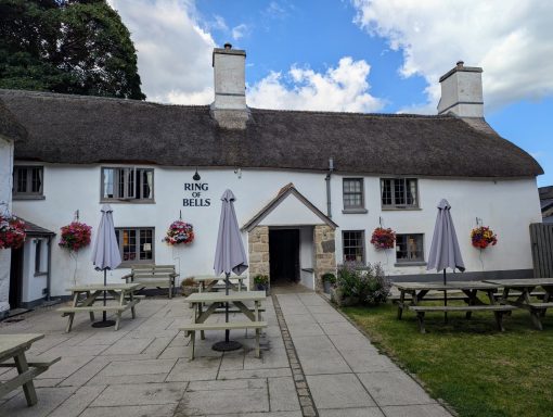 Traditional thatched-roof pub with outdoor seating and flower baskets.