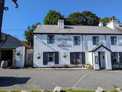 White-washed pub with a sign, surrounded by trees and blue sky.