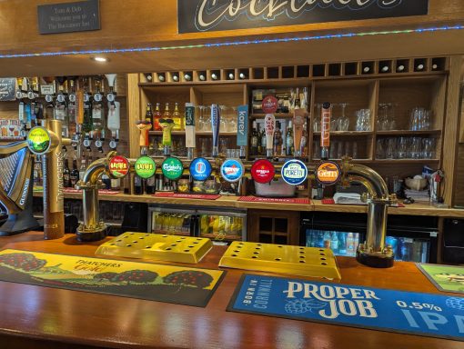 A wooden bar with various beer taps and drinks displayed in a pub setting.