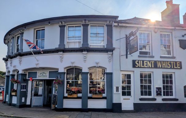 Exterior of a pub named "Silent Whistle" with a curved facade and Union Jack flag.