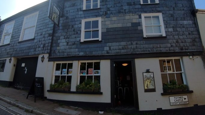 Historic building with slate exterior, featuring a pub entrance and window planters.