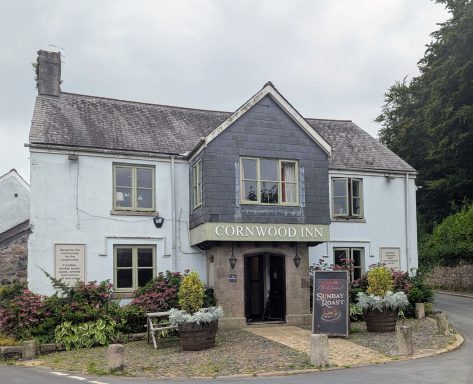Charming pub with a grey exterior, surrounded by greenery and floral decor.