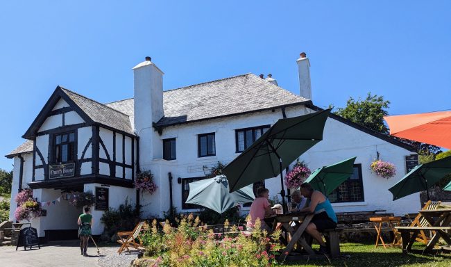 A quaint pub with outdoor seating and umbrellas against a clear blue sky.