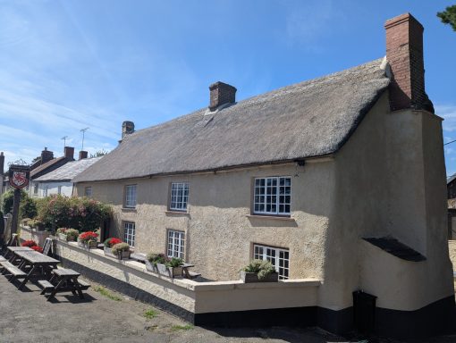 Traditional thatched cottage with flower boxes and benches outside. Clear blue sky.